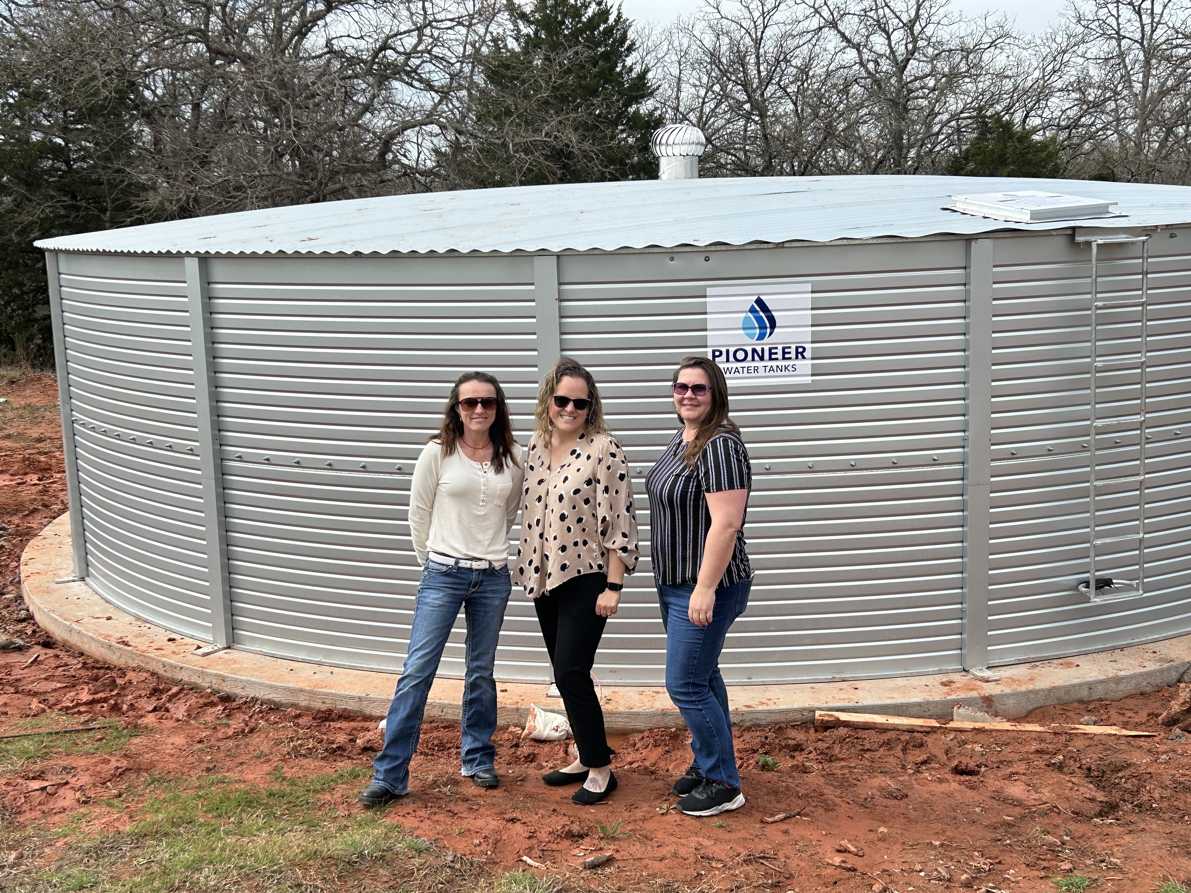 3 tribal women in front of completed 40,000 gal rainwater harvesting tank project.