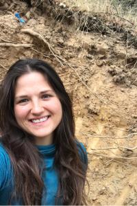 A young woman stands, smiling, in front of a dirt hill.