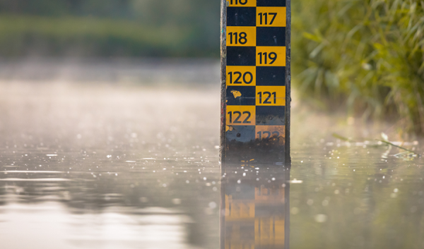 A lake fills the foreground as a black and orange measuring tool displays the depth of the water.